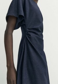Navyblaues Kleid aus strukturiertem Stoff mit kurzen, gepufften Ärmeln und Raffung an der Seite für eine figurbetonte Silhouette.