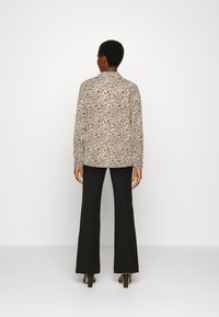 Casaco de estampa de leopardo, feito de um tecido suave, com um corte descontraído e mangas longas, combinado com calças pretas de perna larga e saltos.