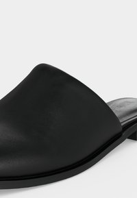 Mule en cuir noir sans talon avec un petit talon et un bout arrondi, présentée sur un fond blanc uni.