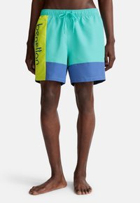Turquoise zwemshorts met een gele zijpaneel en een marineblauwe onderkant. Voorzien van een elastische tailleband en trekkoord. Bedrukt logo langs de zijkant.