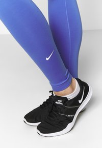 Nike legíny s modrým gradientem a bílým logem, doplněné černými běžeckými botami s bílými akcenty a strukturovaným síťovinovým svrškem.