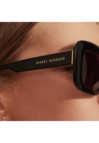 Schwarze übergroße Sonnenbrille mit markantem, eckigem Rahmen. Goldene Markeninschrift "ISABEL BERNARD" an den Bügeln, getönte Gläser und glänzende Oberfläche.