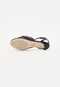 Chaussure slingback en cuir noir avec un bout arrondi et une sangle délicate. Semelle texturée avec un léger talon. Détail de couture remarquable sur la tige.