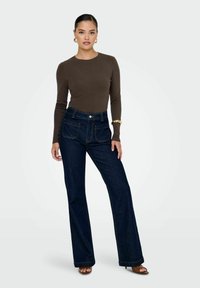 Jeans flared in denim blu scuro con vita alta e tasche frontali, abbinati a un top fitted marrone a maniche lunghe e sandali con tacco.