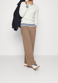 Hvid strikket sweater med blå striber ved kraven og kanten, lysebrune plisserede bukser og hvide sneakers med marineblå detaljer.