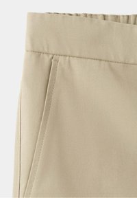 Gros plan sur un pantalon en tissu coton beige avec poche avant et couture renforcée à la ceinture.