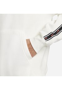 Vit huvtröja med framficka, med en texturerad finish och svart och röd randdetalj längs ärmen.