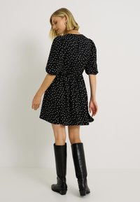Vestido negro con lunares, mangas cortas abullonadas, cintura ajustada y falda acampanada, combinado con botas de cuero negras hasta la rodilla.
