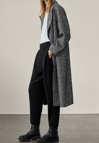 Zwart-witte geblokte lange jas met een relaxte pasvorm, gecombineerd met een witte top en zwarte geplooide broek; enkelhoge zwarte laarzen.
