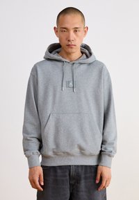 Sudadera gris hecha de tela suave, con un bolsillo tipo canguro, cordones ajustables y un parche con el logo en el pecho.