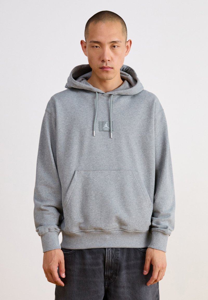 Sudadera gris hecha de tela suave, con un bolsillo tipo canguro, cordones ajustables y un parche con el logo en el pecho.