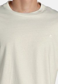 Kortærmet t-shirt med rund hals i blød beige stof med let tekstur og et lille hvidt logo på venstre brystområde.