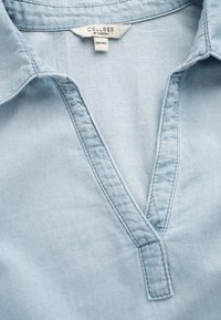 Ljusblå bomullskjorta med V-ringning, veckad krage och enkla sömnadsdetaljer. Etikett med texten "CELLBES OF SWEDEN", storlek 38/40.