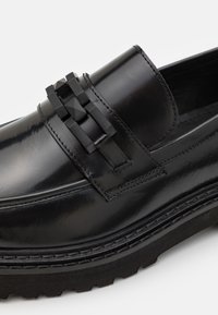 Sorte skinn Loafers med en blank finish, tykk gummisåle og en dekorativ stropp med matte svarte detaljer. Synlig stingdetaljering.