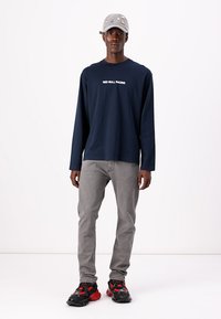 Camisa de manga larga de la Marina con el texto "RED BULL RACING", jeans grises y zapatillas texturizadas negras y rojas. Gorra gris con adornos.