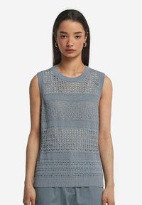 Ljust blå stickad ärmlös topp med strukturerade mönster och öppna mesh-designs. Ribbad halsringning och nederkant ger struktur.