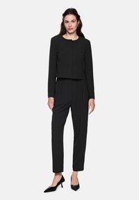 Black tailored cropped jacket with long sleeves paired with high-waisted black trousers, complemented by pointed black heels.
