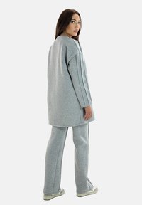 Grijs oversized sweatshirt en bijpassende broek van zacht, textuurstof, met zijsplitten en een relaxte pasvorm. Eenvoudig ontwerp, neutrale kleur.