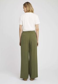 Pantalons larges en tissu vert olive, avec une texture lisse, taille haute et deux poches arrière, associés à un t-shirt blanc uni.