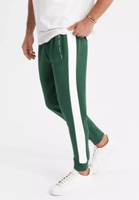 Gröna träningsbyxor med vita sidostråkar, med en figurnära design och elastiska muddar. Bärs med vita sneakers för en sportig look.