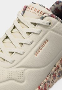 Ανοιχτόχρωνο αθλητικό παπούτσι Skechers με σόλα και γιακά σε μοτίβο με λουλούδια, δερμάτινη υφή, επίπεδα κορδόνια και λογότυπο Skechers στη γλώσσα και στο πλάι.