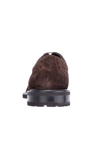 Hnědé semišové boty se zaoblenou špičkou, zdobené dekorativním švem a texturovanou černou gumovou podrážkou. Pohled zezadu ukazuje zakřivení boty.