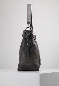 Szara skórzana torba o ziarnistej fakturze, charakteryzująca się zwartym kształtem, odpinanym paskiem i elegancką czarną podstawą. Widoczny detal zamka błyskawicznego.