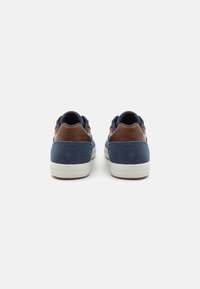 Blue denim sneakers with brown leather accents, white rubber soles, and round laces. Back view highlighting logo on heel.