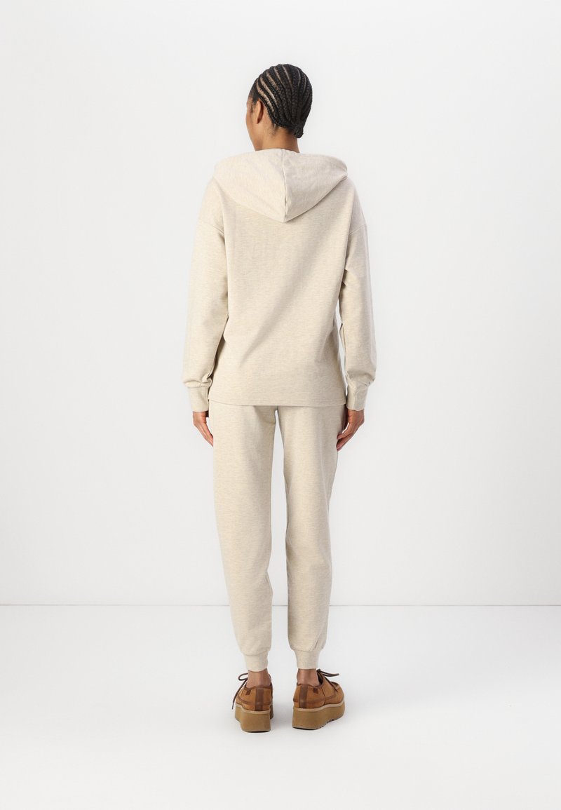 Helle beige Kapuzenjacke mit Kordelzug, kombiniert mit passenden, schmal zulaufenden Jogginghosen. Strukturiertem Stoff mit gerippten Bündchen. Braune Plateauschuhe.