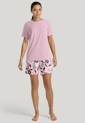 T-shirt rose clair à manches courtes associé à un short à motifs floraux dans des teintes de rose, vert et noir ; tissu lisse, coupe décontractée.