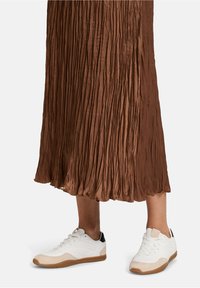 Baskets blanches avec une finition texturée, dotées d'un accent de talon noir et d'une semelle extérieure beige clair, associées à une jupe plissée marron.