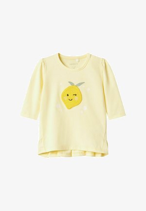 Chemise à manches longues jaune avec un appliqué de citron souriant, des accents floraux et un col arrondi. Tissu en coton doux avec un détail froncé aux manches.