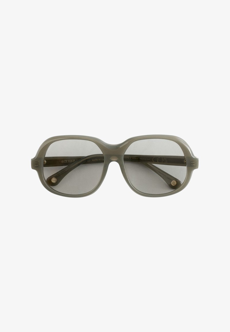 Lunettes de soleil carrées surdimensionnées translucides grises avec des bords légèrement arrondis et des verres teintés, vues de face.