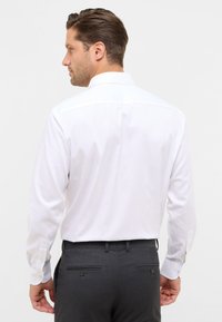 Witte langslavige dressshirt met subtiele verticale strepen, standaard kraag en knoopmanchetten, gecombineerd met donkergrijze op maat gemaakte broeken.