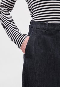 Σκούρο τζιν παντελόνι με πλαϊνές τσέπες, φορεμένο με ένα μαύρο και άσπρο ριγέ πουλόβερ με μακριά μανίκια. Είναι εμφανές το υφασμάτινο σχέδιο και η κομμένη εφαρμογή.