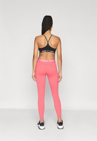 Μαύρο αθλητικό σουτιέν με λογότυπο. Φωτεινές ροζ κολάν με λωρίδα με σχέδιο στη μέση. Λευκά αθλητικά παπούτσια με μαύρες λεπτομέρειες.