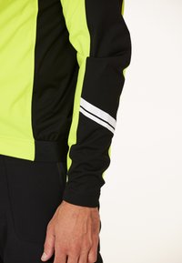 Långärmad träningsjacka med klara neon gula och svarta paneler, med en vit accentrand på den svarta ärmen. Slät textil.