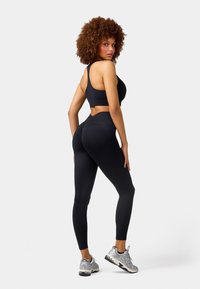 Black sports bra and leggings set featuring a cutout at the waist. The fabric appears smooth, fitted, and stretchy, paired with silver athletic shoes.