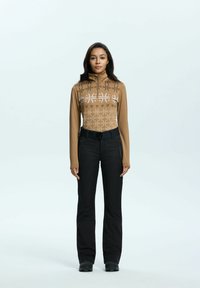 Bruine zip-up top met geometrische patronen in het wit, gecombineerd met zwarte broek met een riem en zijzakken. Soepele textuur, aansluitend ontwerp.