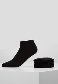 Schwarze Knöchelsocken aus Baumwollmischung, mit einem gerippten Bund und glatter Textur, daneben ein Stapel Socken, von denen eine aufrecht steht.