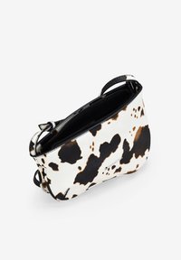 Bolso de mano con diseño de piel de vaca en tonos blanco y negro, que cuenta con un cierre con cremallera, dos asas y una textura suave.