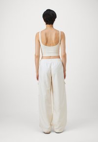 Svetlo béžový rebrovaný crop top s tenkými ramienkami, skombinovaný s voľnými krémovými nohavicami s vysokým pásom, ktoré majú bočné vrecká a elastický pás.