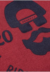 Rode stof met een gestructureerd oppervlak en zwarte grafische ontwerpen, waaronder een gestileerde baard en het nummer "20" dat duidelijk zichtbaar is.