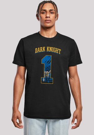 Svart bomull t-skjorte med "DARK KNIGHT" i gul tekst og en blå grafikk av en karakter med kappe og flaggermussymbol. Løs passform.