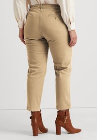 Beige ankle-length pants with a smooth texture, two back pockets, and a fitted waist, paired with brown high-heeled ankle boots.