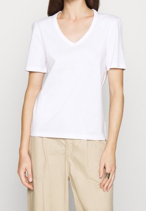 Weißes Baumwoll-T-Shirt mit kurzen Ärmeln und V-Ausschnitt. Glatte Textur, leicht lockere Passform, kombiniert mit beigen Hosen und einem Ring.