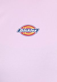 Šviesiai rožinė medvilninė marškinėliai, su apvaliu daugiaspalviu logotipu, kuriame centre yra „Dickies“ tekstas. Lygus paviršius.