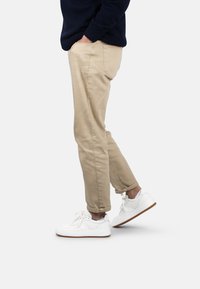 Chinos beiges avec une coupe droite, des poignets retroussés et des poches latérales. Portés avec des baskets blanches à tige en cuir texturé.