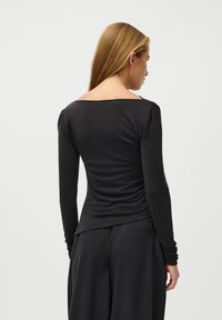 Crna majica s dugim rukavima, širokim izrezom i krojem koji naglašava tijelo. Mekani, rastezljivi materijal s suptilnim nabranjima uz ramena i donji rub.