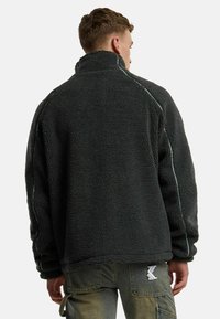 Tumehall fleece'i pullover-jakk, millel on kõrge krae, tekstureeritud pind ja kontrastsed valged õmblused õlgadel.